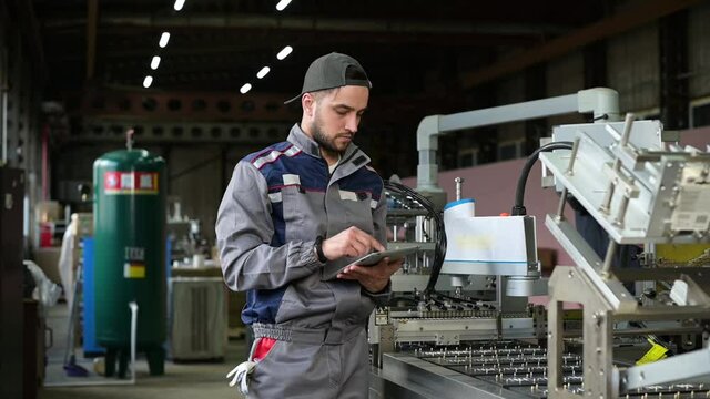Portrait of a young worker in an assembly line at a battery factory. Slow motion, young man in work clothes at production