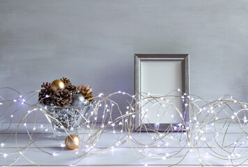 Christmas decoration, mock up in a white frame with cones and christmas lights on a white table, copy space