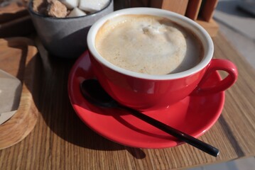 A red mug with coffee glanced at the saucer on the table.