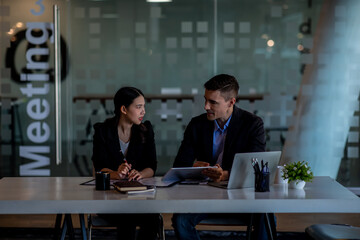 Business people working together. Serious businessman with laptop talking to a businesswoman with papers and tablet. Business partners have a successful meeting in the modern office.
