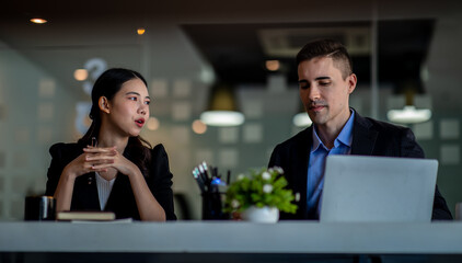 Business people working together. Serious businessman with laptop talking to a businesswoman with papers and tablet. Business partners have a successful meeting in the modern office.