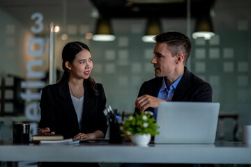 Business people working together. Serious businessman with laptop talking to a businesswoman with papers and tablet. Business partners have a successful meeting in the modern office.