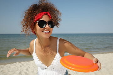 Happy African American woman throwing flying disk at beach on sunny day