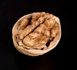 A whole beautiful walnut kernel in half a walnut shell on a black background