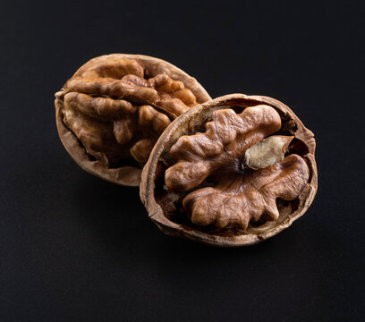 Two cracked walnuts. Beautiful textured walnut kernels in a dark textured shell on a black background