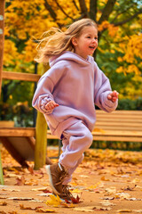 Fototapeta premium The girl went down the hill. The child plays on the playground in the fall. Wooden platform on the territory of the new house. Happy childhood. Yellow foliage on the trees on a sunny day.