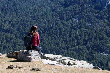 Naklejka na ściany i meble Mujer joven descansando después de una subida de hiking admirando los pinares de la montaña. mirador de los Canchos en la Sierra de Guadarrama en Madrid, España.