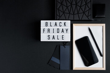 Black Friday online sale concept. Monochromatic flatlay on dark background. Smartphone and accessories.