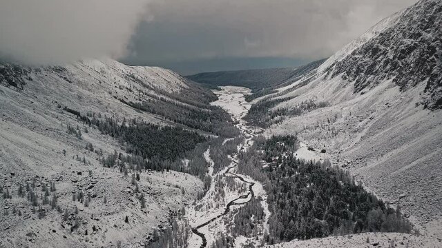 The foot of the glacier of the huge Belukha mountain, the valley of the Aktru River, the Altai mountains. Cloudy weather, storm, wildlife, winter forest, frozen mountain river in the valley of the