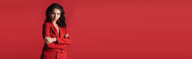 young brunette model in suit posing with crossed arms isolated on red, banner.