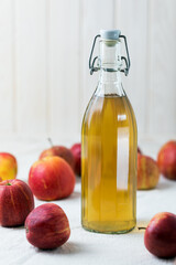 Bottle of apple cider vinegar on a light background, next to fresh apples