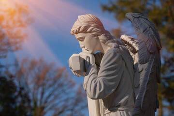 Profile of an ancient statue of angel with cross in sun rays as symbol of Christianity, death and...