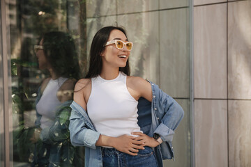 Attractive asian girl walking along streets of modern city, leaning against glass wall. Teenager...