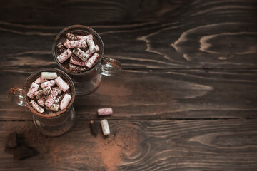 Two glasses of hot cocoa or coffee with marshmallows on a wooden table. Warming coffee drink. Composition in dark style with copy space. View from above.