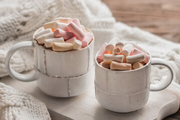 Two cups of hot coffee drink with marshmallows and a warm white scarf on a wooden table. Cozy winter morning.