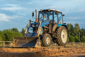 A blue tractor with a bucket stands on a construction site on a farm