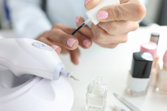 Woman doing her own manicure with pink nail polish closeup