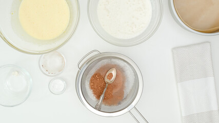 Whipped whites, whipped yolks, and cocoa powder close up on kitchen table. Step by step chocolate cake recipe, flat lay, white kitchen table background