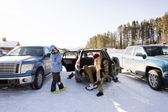 Friends preparing for snowboarding at car in snowy sunny parking lot