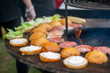 Burger buns and patties are grilled outdoors. Burger bbq