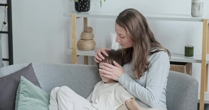 Caring young mother calm down and hugging little adorable son sitting together on couch at home interior. Woman taking care support embracing cute male kid. Parent worried attention anxiety to child