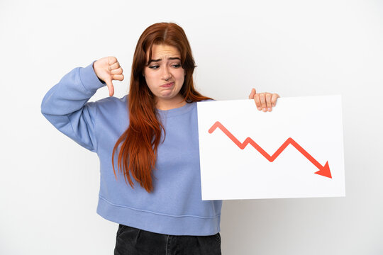 Young redhead woman isolated on white background holding a sign with a decreasing statistics arrow symbol and doing bad signal