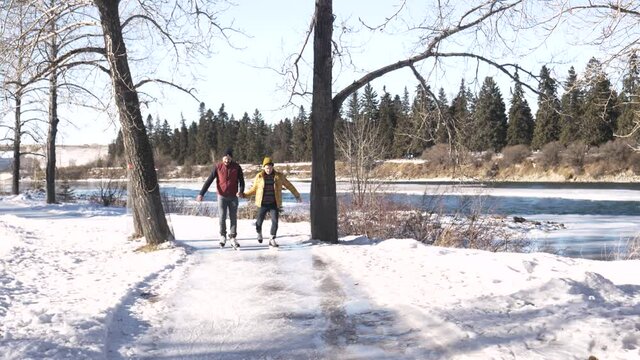 Gay Male Couple Holding Hands Ice Skating On Frozen Path In Park