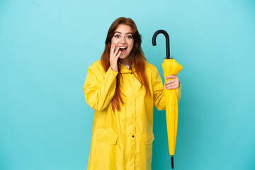 Redhead woman holding an umbrella isolated on blue background with surprise and shocked facial expression