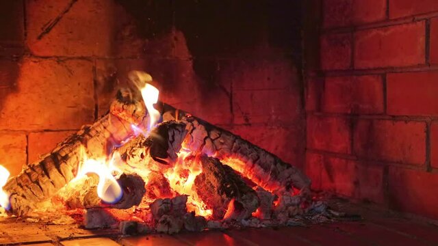 Burning logs and embers in a clay brick fireplace in a country cottage
