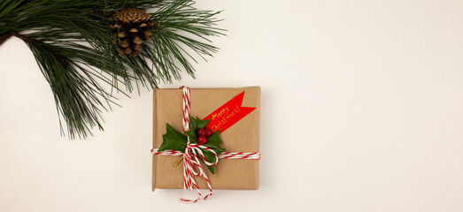 hand-made Christmas gift wrapped in craft paper and decorated with a sprig of holly on a white background. Christmas traditions. Winter holidays.
