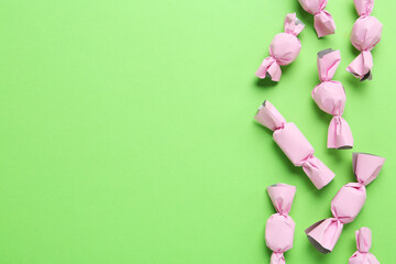 Many candies in light pink wrappers on green background, flat lay. Space for text