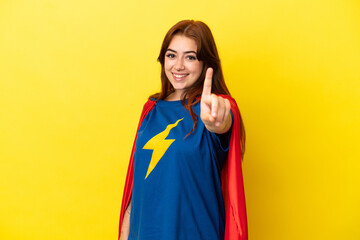 Super Hero redhead woman isolated on yellow background showing and lifting a finger