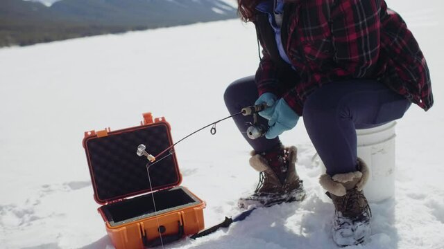 Senior woman ice fishing on frozen alpine lake
