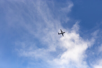 Flying turboprop plane on a background of blue sky with light white clouds.