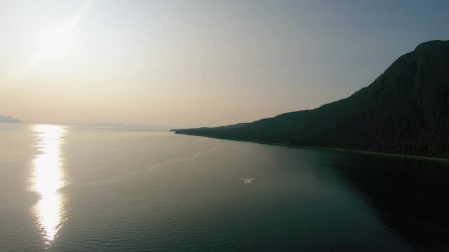 Aerial top shot flying over amazing sea with sun glare and high mountains at summer sunset amazing view. Shooting from helicopter beautiful nature landscape.
