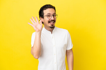 Young caucasian man isolated on yellow background saluting with hand with happy expression
