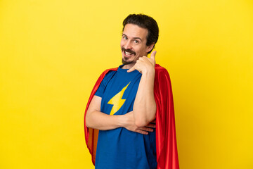 Young caucasian man isolated on yellow background in superhero costume and doing phone gesture © luismolinero