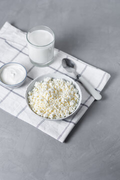 Homemade cottage cheese with glass of milk, spoon in bowl on light background. Healthy dairy products, baking ingredients. Source of calcium for breakfast, diet food