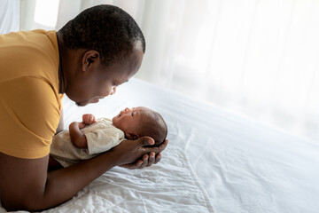 An African American father used both hands to support his son's head, 12-day-old baby black skin newborn son, lying in bed in a bedroom with happy and protection, concept to African family and newborn