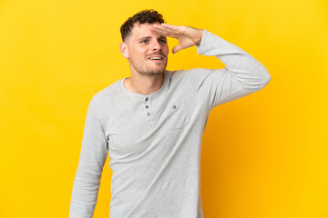 Young caucasian handsome man isolated on yellow background looking far away with hand to look something