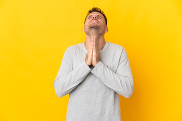 Young caucasian handsome man isolated on yellow background keeps palm together. Person asks for...
