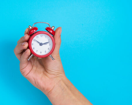 Alarm clock red color in woman hand on bright blue background