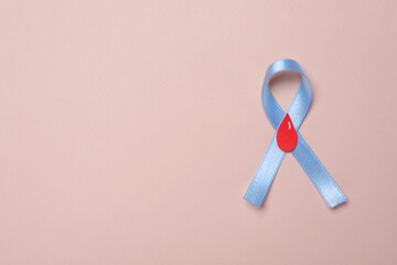 Light blue ribbon with paper blood drop on pale pink background, top view and space for text....