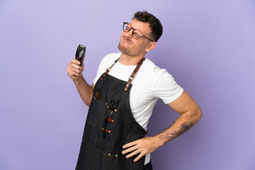 Naklejka premium Barber caucasian man in an apron isolated on purple background suffering from backache for having made an effort