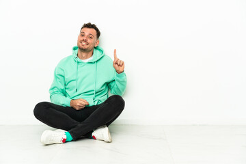 Fototapeta premium Young handsome caucasian man sitting on the floor pointing with the index finger a great idea