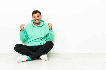Fototapeta premium Young handsome caucasian man sitting on the floor celebrating a victory in winner position