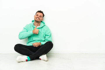 Young handsome caucasian man sitting on the floor giving a thumbs up gesture