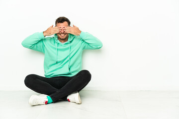 Young handsome caucasian man sitting on the floor covering eyes by hands