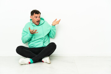 Obraz premium Young handsome caucasian man sitting on the floor with surprise facial expression
