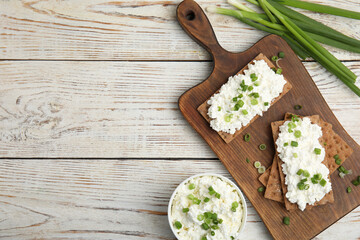 Crispy crackers with cottage cheese and green onion on white wooden table, flat lay. Space for text